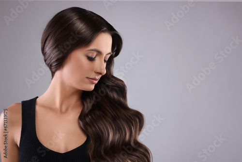 Gorgeous woman with shiny wavy hair on grey background, space for text. Professional hairstyling