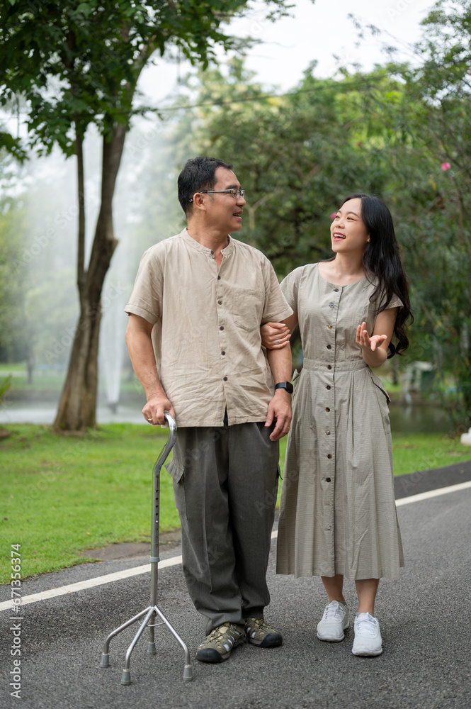 Happy senior Asian dad is talking with his lovely daughter while walking in the green park daughter.