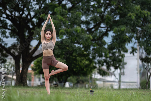 Young healthy Asian woman stretch her body on a yoga mat. Do yoga in a lush park Yoga and Pilates concept © wichayada