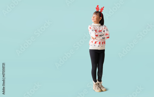 Cheerful young Asian girl wearing a Christmas sweater with reindeer horns, Happy smiling standing with Looking surprise posing full body portrait, isolated on blue background