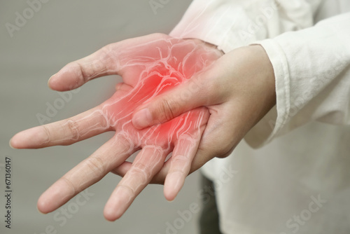 Anonymous person touching her wrist, suferring from arthritis disease, close up against grey background
