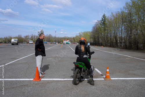 A young woman is learning to ride a motorbike in a motorcycle school. She is taught by a teacher