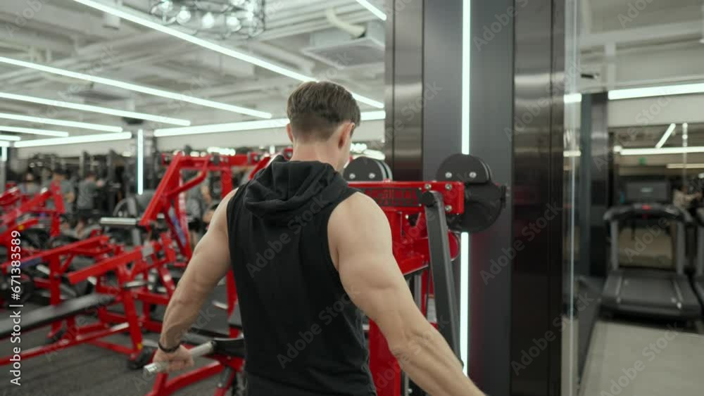 Mascular Adult Male Perform Shoulder Side Raise Exercise in Machine at Fitness Center - rear view Mascular Adult Male Perform Shoulder Side Raise Exercise in Machine at Fitness Center - rear view