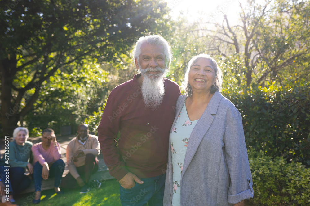 Happy biracial couple of senior friends embracing and smiling in sunny garden