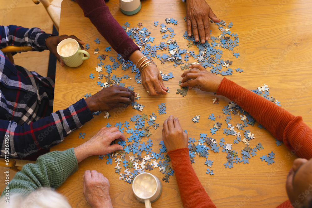 Fototapeta premium Hands of diverse group of senior friends playing with jigsaw puzzles in sunny dining room at home