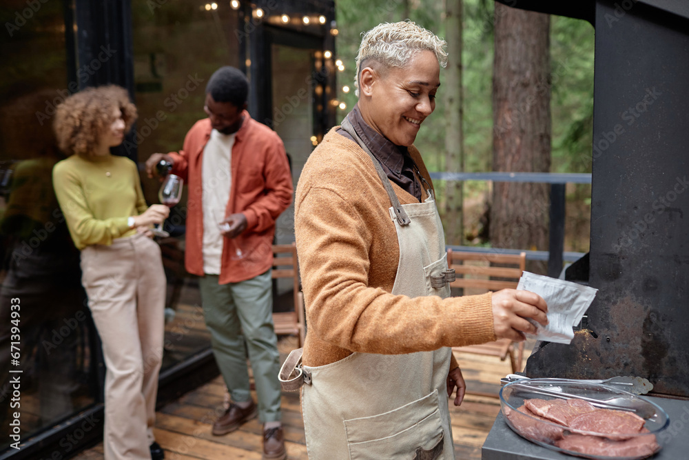 Young smiling woman cooking meat on grill at barbecue party Young smiling woman cooking meat on grill at barbecue party