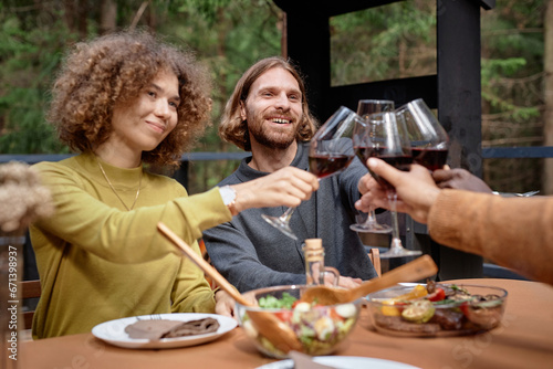 Young couple celebrating with their friends, they sitting at table and drinking red wine at party outdoors