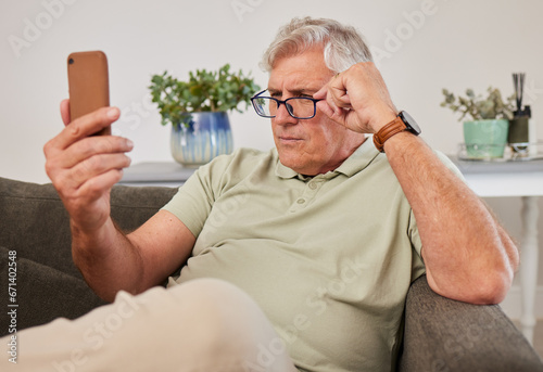 Phone, glasses and senior man reading a text message, blog or online news on a sofa in the living room. Vision, technology and elderly male person squinting while networking on a cellphone at home.