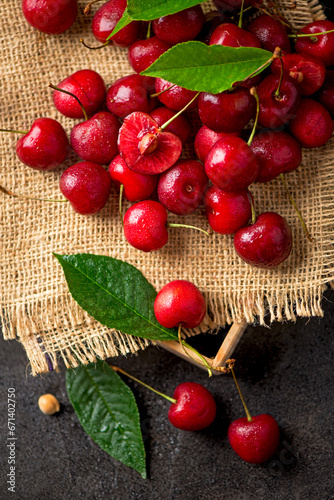 Sweet red cherry on burlap on a black background. A large number of cherries with leaves on the table, on a black background. close-up.