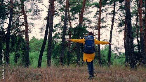 Woman with backpack runs spreading arms among fir forest on autumn day