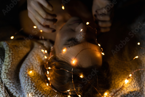 The head and hands of a reclining woman with many Christmas lights photo