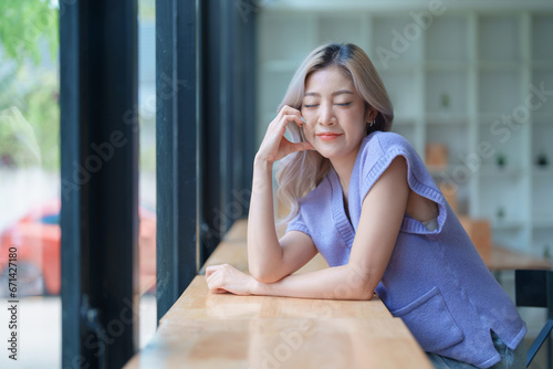 Asian young woman making notes in paper notebook sitting on cozy sofa on background of window. Pretty female writing notes in diary or making to do list relaxing at home.