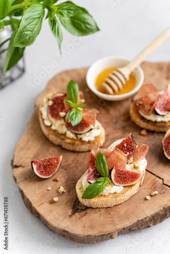 Tasty bruschetta with ciabatta baguette, Parma ham or prosciutto, cream cheese, figs, basil, honey and walnut on wooden board on white background. Antipasti. Vertical, close up. Canape, sandwiches