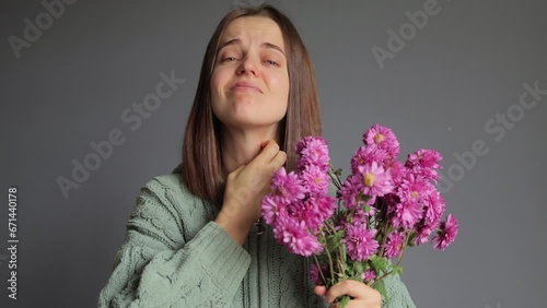 Pollen season. Rhinitis reaction. Chrysanthemum allergy. Seasonal disease. Sick woman wearing green knitted shirt holding bouquet in hands, isolated over gray background suffering neck itch photo