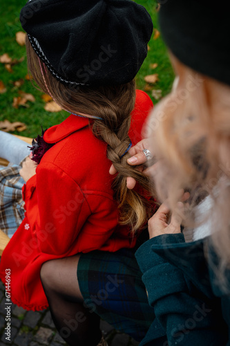 Mother braids her cute daughter's hair on a warm autumn day
