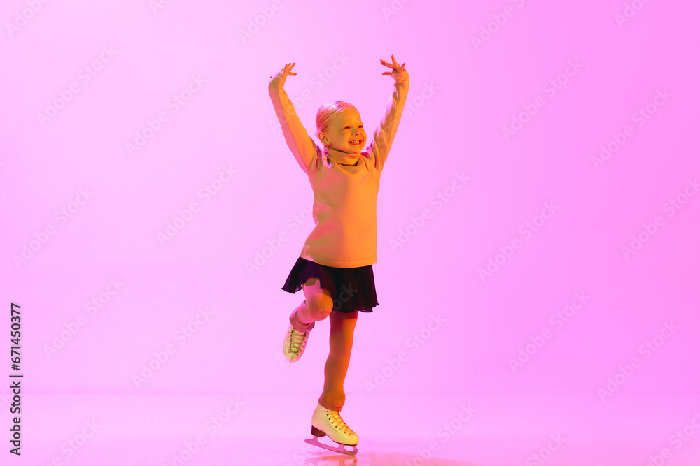 Smiling, happy, positive little kid, old girl in sweater and skirt, dancing on skates against pink background in neon light. Concept of childhood, figure skating sport, hobby, school, education