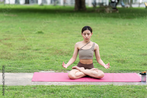 Asian woman in sporty outfit relaxing meditating feeling zen like on fitness mat in public park outdoor. Healthy active lifestyle