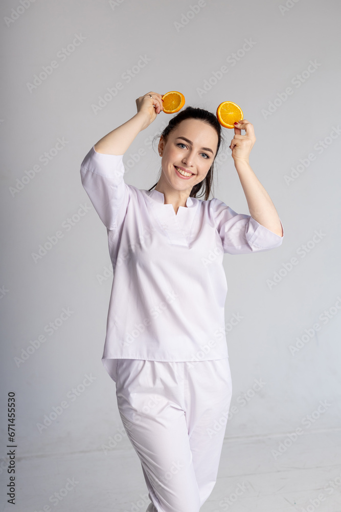 
Portrait of an attractive young woman posing with a sliced ​​orange on a gray background. Girl with an orange on a gray background. game with fruits. Bright orange. Vitamin C