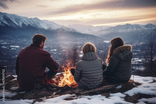Friends sitting around campfire in evening during mountain winter trip. Winter season. Weekend trip. Travel to the mountains