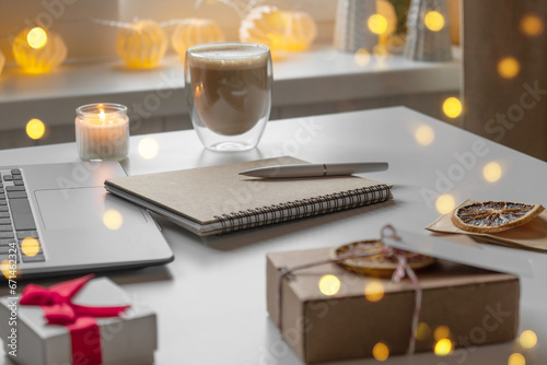 Notepad with a pen, laptop, coffee cup, wrapped gifts on a desk table. Winter Festive atmospheric mood. Preparation for Christmas. Business Holidays Concept. Freelancer's desktop during Xmas vacation