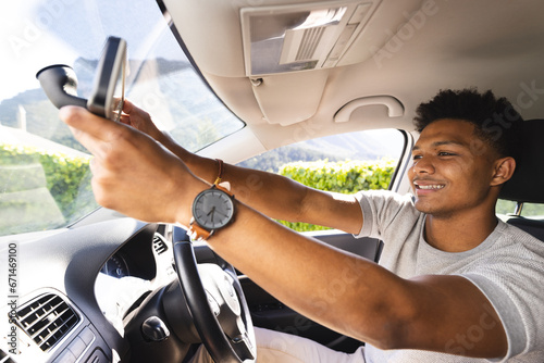 Happy african american man adjusting rearview mirror in car on sunny day photo