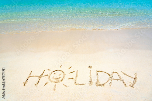 Holiday hand written in the sand on the beach blue waves in the background. Sun drawing on golden sand beach, holiday background sign concept.
