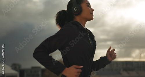 Fitness, music and a woman running in the city for health or cardio preparation of a marathon. Exercise, wellness or sports training and a young runner or athlete listening to audio with headphones