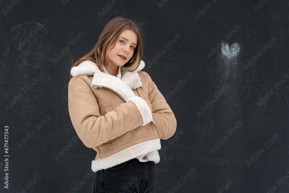 Pretty young woman in short beige sheepskin coat poses in studio on black background. Space for text. Casual look Pretty young woman in short beige sheepskin coat poses in studio on black background. Space for text. Casual look