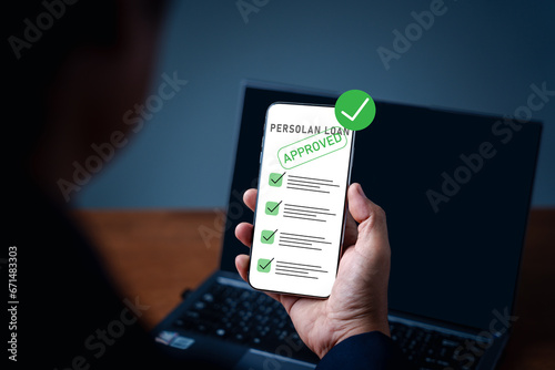 A man uses phone to check the status of his personal loan application. Loan approval from a bank or company that allows individuals or organizations to borrow money for business or personal expenses photo