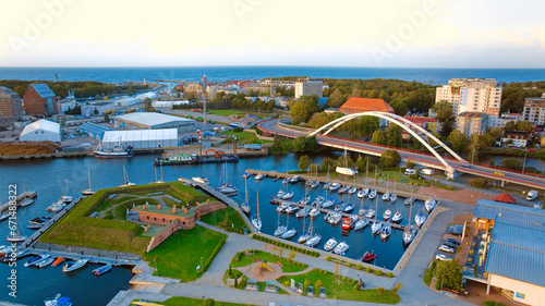 A breathtaking aerial drone photo of Kołobrzeg's marina in Poland captures a picturesque scene. The view showcases a multitude of yachts, sailboats, fishing boats and ships.