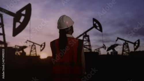 Back View Of Asian Female Engineer Talking On Smartphone Inspects Oil Pumps 
 photo