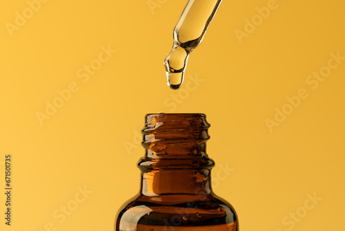 Close up of glass bottle and pipette with drop and copy space on yellow background photo