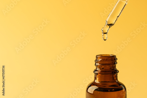 Close up of glass bottle and pipette with drop and copy space on yellow background