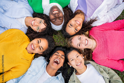 Multiracial group of young women in circle smiling at camera together - Happy girlfriends having fun lying on the grass at the park - Female community and friendship concept - Women power