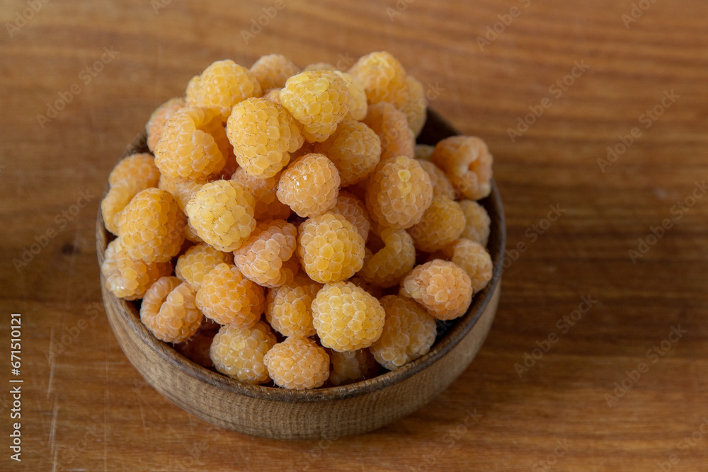Yellow raspberries in a wooden bowl on the table. Summer berries background. Vitamin food, berry harvest. Healthy nutrition. Yellow raspberries in a wooden bowl on the table. Summer berries background. Vitamin food, berry harvest. Healthy nutrition.