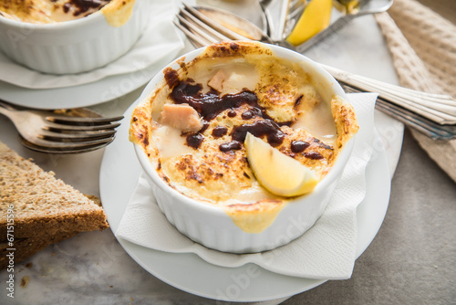 Typisches DDR Würzfleisch Ragout Fin mit Käse überbacken, Zitrone, Toast Brot und Worcester Sauce  in Auflaufform Schale auf Marmor Teller und hell grau Stein Hintergrund