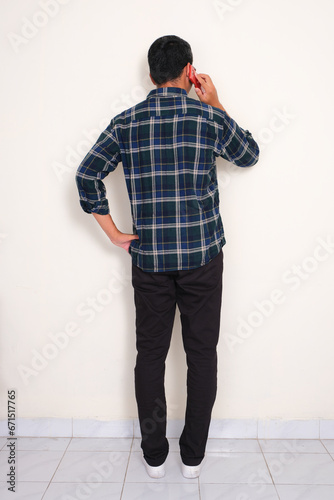 Full body rear view portrait of a man standing while answering a phone call