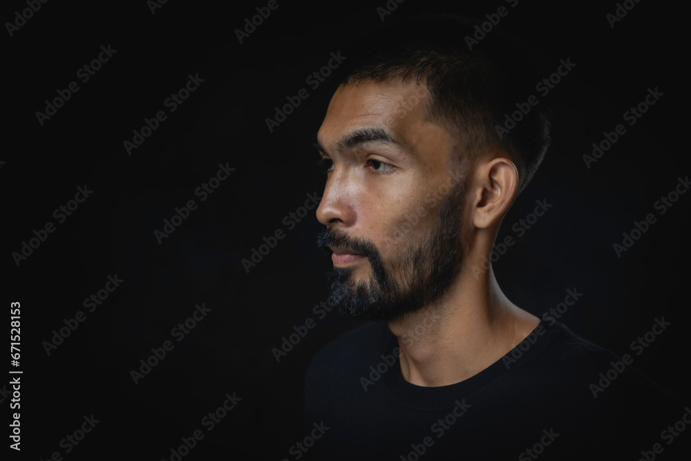 Portrait serious young man with beard looking away against a black background