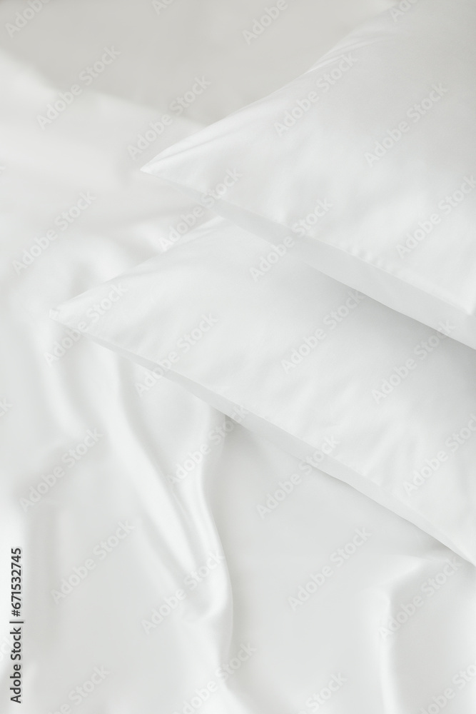 Obraz premium Two white pillows in satin or silk or lyocell pillowcases on white sheet. Bedding and accessories. Home textile