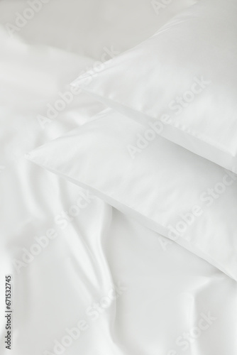 Two white pillows in satin or silk or lyocell pillowcases on white sheet. Bedding and accessories. Home textile © Мария Крузман