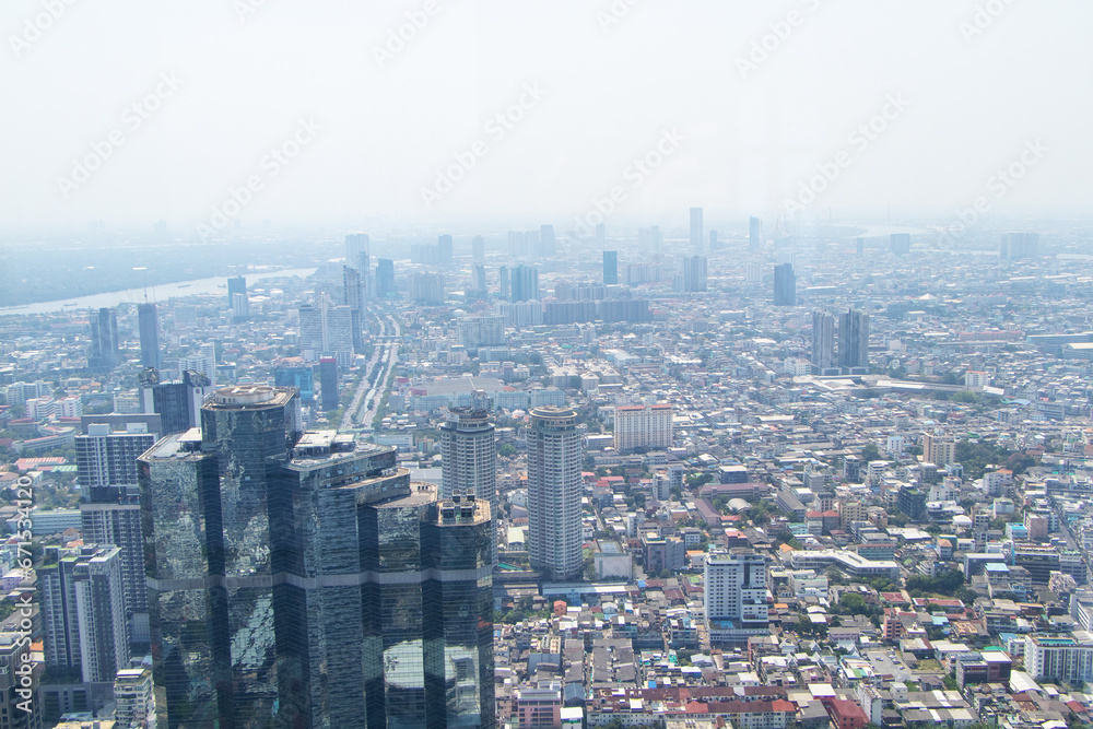 Scenery aerial view on top of buildings in town Bangkok, Thailand city with air cloudy by fog or air pollution in evening with hotels and office towers . White sky was blurred with bright sunlight.