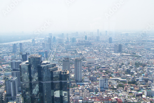 Scenery aerial view on top of buildings in town Bangkok, Thailand city with air cloudy by fog or air pollution in evening with hotels and office towers . White sky was blurred with bright sunlight.