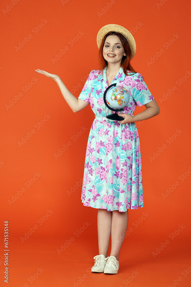 Woman looking at the camera smiling, holding small globe and showing empty area with hand, isolated on orange background. Portrait of female traveler. Woman looking at the camera smiling, holding small globe and showing empty area with hand, isolated on orange background. Portrait of female traveler.