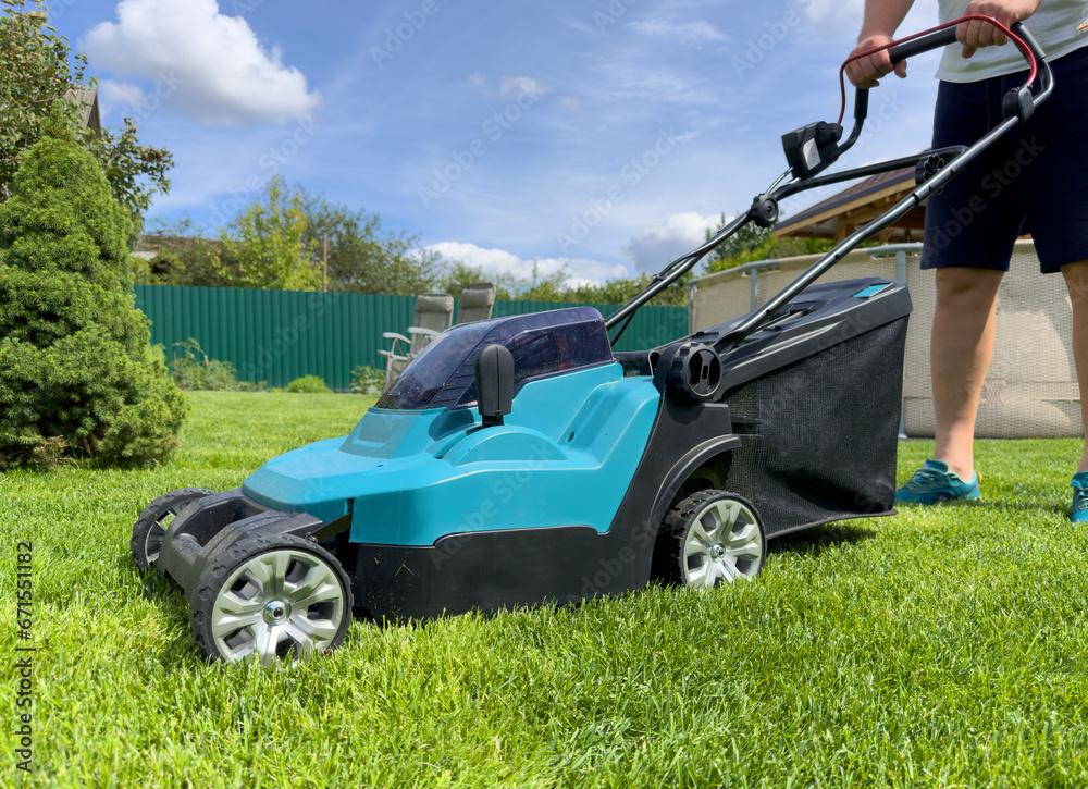 Lawn Mower Electric for cutting grass in garden. Сutting grass in yard using Lawn Mower. Lawn mowing machine. Grass Trimmer and Grass Cutter. Lawn maintenance service. Gardener mows weeds Lawn Mower Electric for cutting grass in garden. Сutting grass in yard using Lawn Mower. Lawn mowing machine. Grass Trimmer and Grass Cutter. Lawn maintenance service. Gardener mows weeds