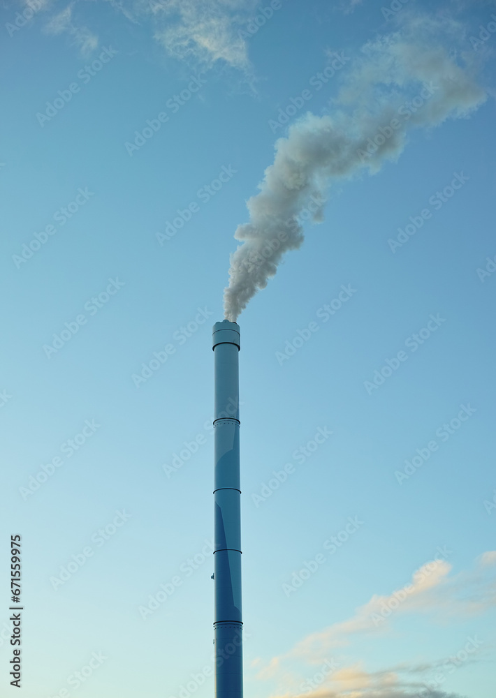 A factory chimney with smoke billowing into the air. Large amounts of steam or smoke billowing from an industrial smoke stack, adding to pollution and air contamination from big industrial industries