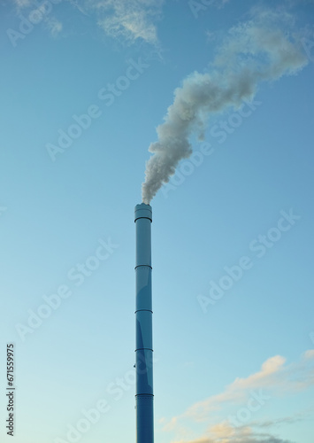 A factory chimney with smoke billowing into the air. Large amounts of steam or smoke billowing from an industrial smoke stack, adding to pollution and air contamination from big industrial industries