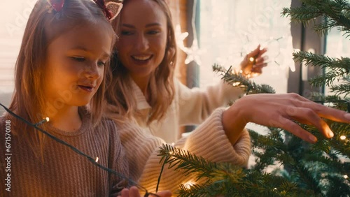 Cheerful mother and daughter decorating Christmas tree with lights. Shot with RED helium camera in 8K.  