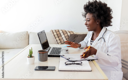 African American woman doctor working at her office doing telemedicine services. Helping patients online and by the laptop. Primary care consultations. photo