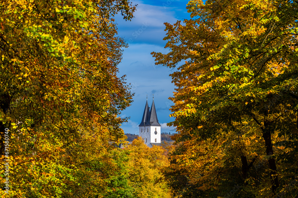Indian summer in Iserlohn Sauerland with twin towers of old Protestant church “Oberste Stadtkirche“ seen through colorful foliage of autumn trees on a sunny october day in Germany. Idyllic atmosphere.