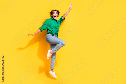 Full length photo of cheerful pretty lady wear green shirt jumping high having fun empty space isolated yellow color background © deagreez